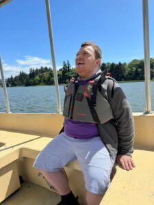 Justen, a young man in a life vest sits on a boat smiling